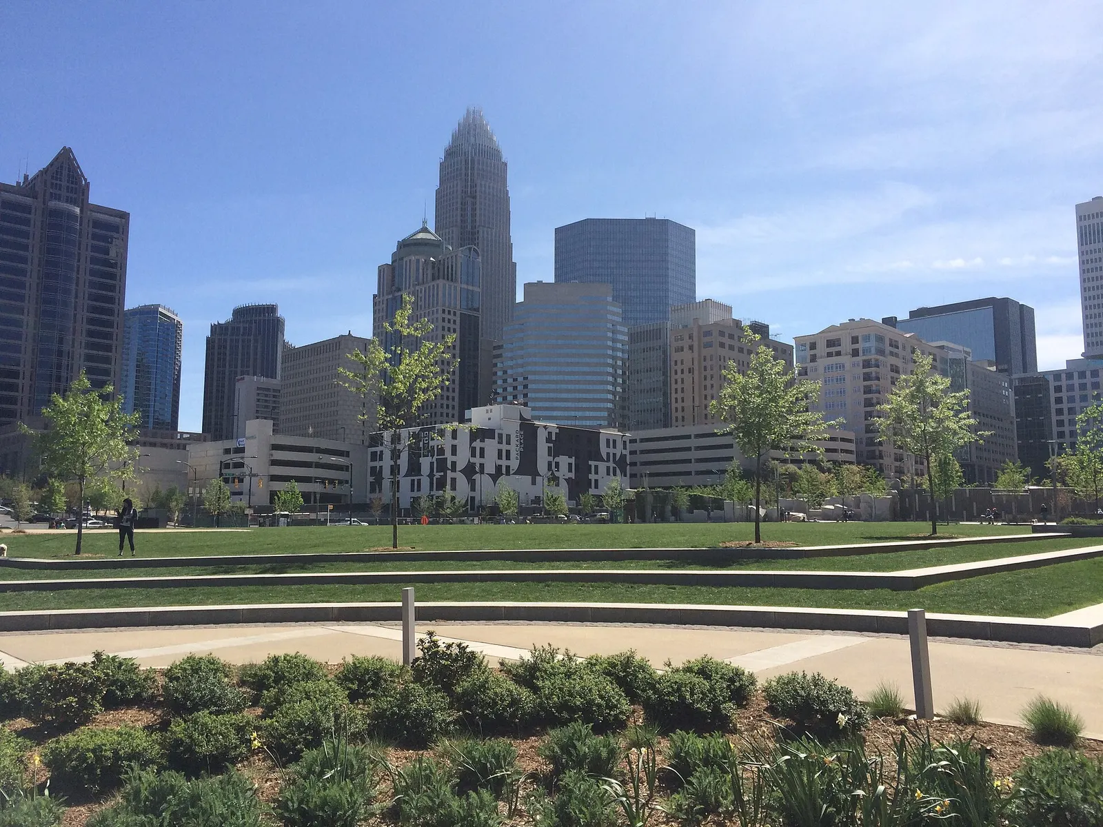 Uptown Charlotte towers rising behind the lawn and young trees of Romare Bearden Park on a clear spring day.