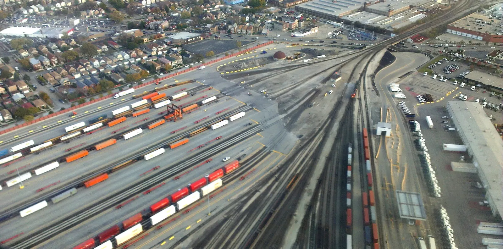Aerial view of a Chicago railyard with rows of orange, white and red intermodal containers on parallel tracks beside houses and warehouses