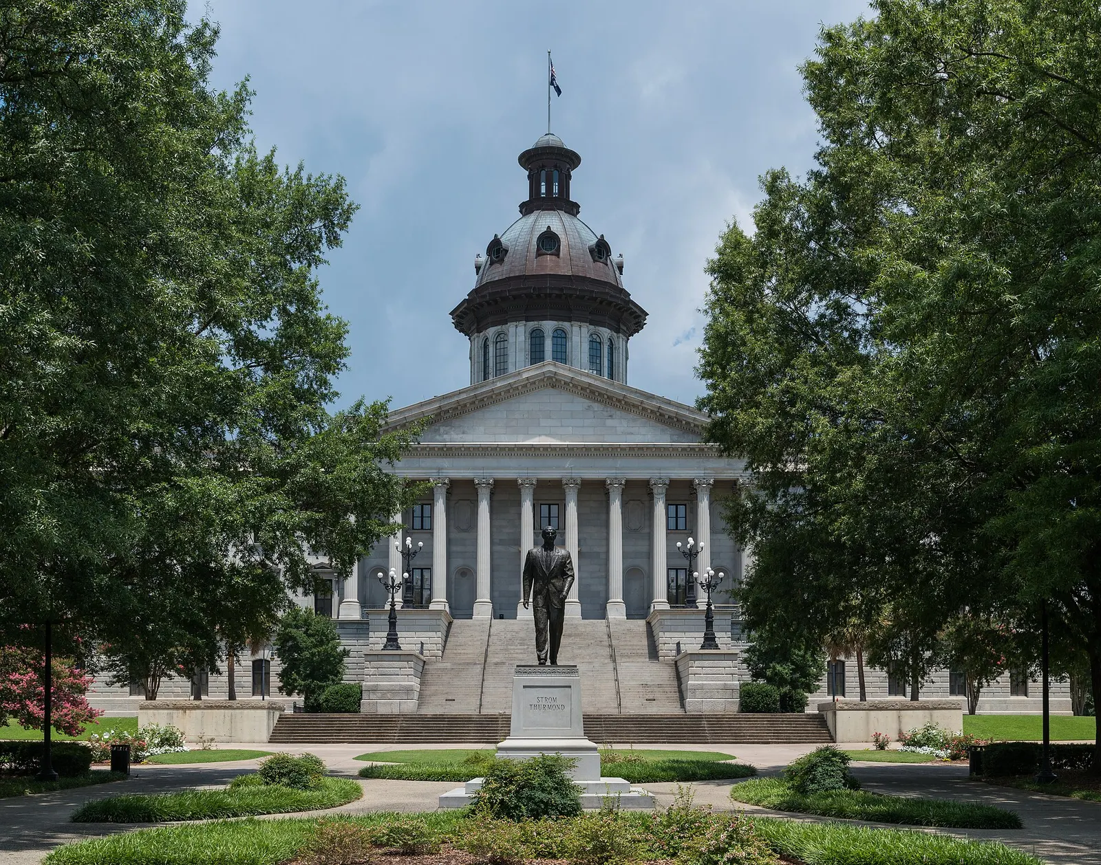 South Carolina State House in Columbia seen between two trees, with a columned front, a copper dome and a bronze statue on the lawn