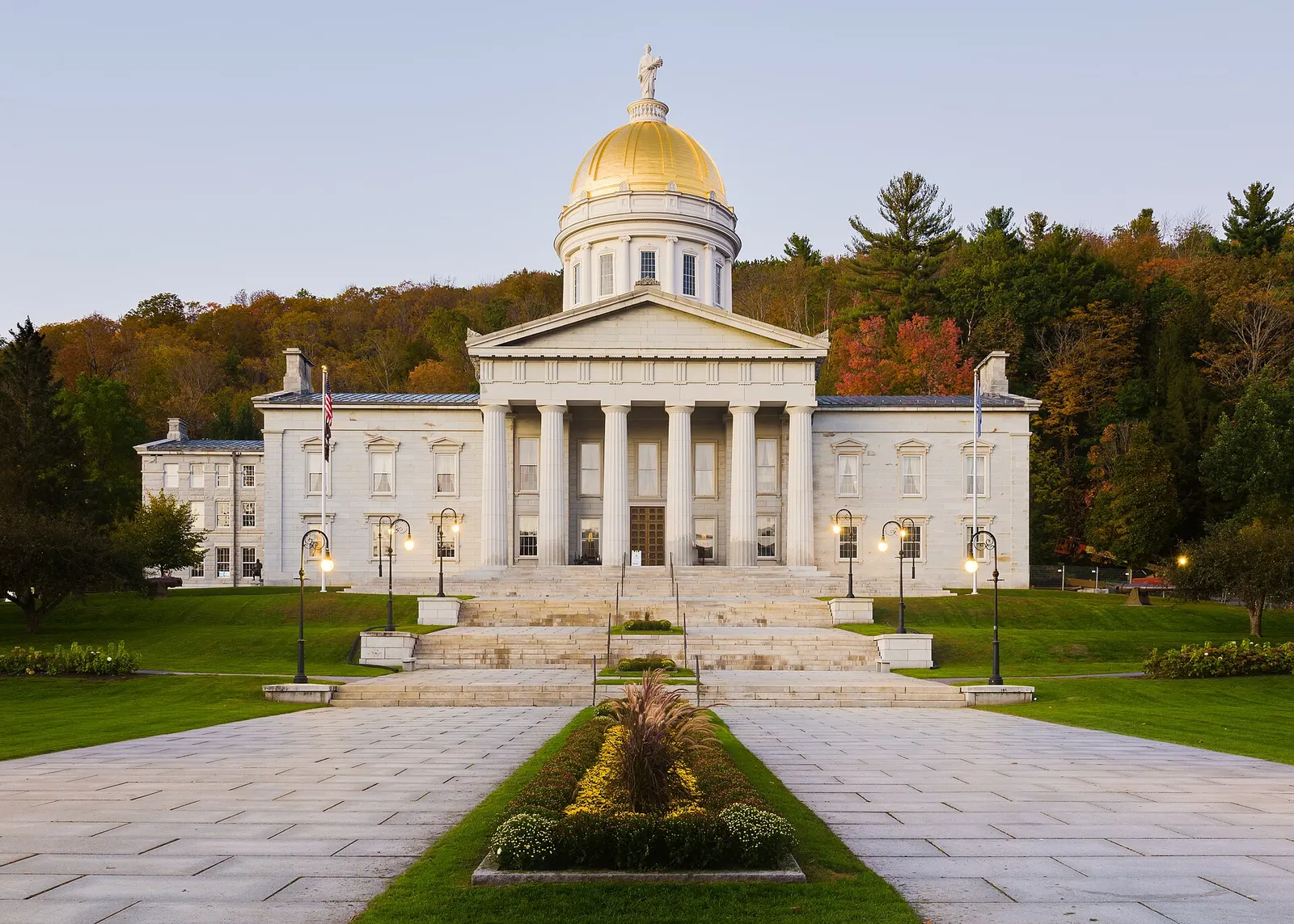 The Vermont State House in Montpelier a pale stone building with a gold dome and columned portico, framed by autumn trees